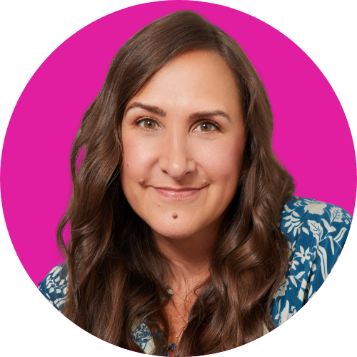 Smiling woman with long brown hair in a blue patterned blouse, against a bright pink circular background.