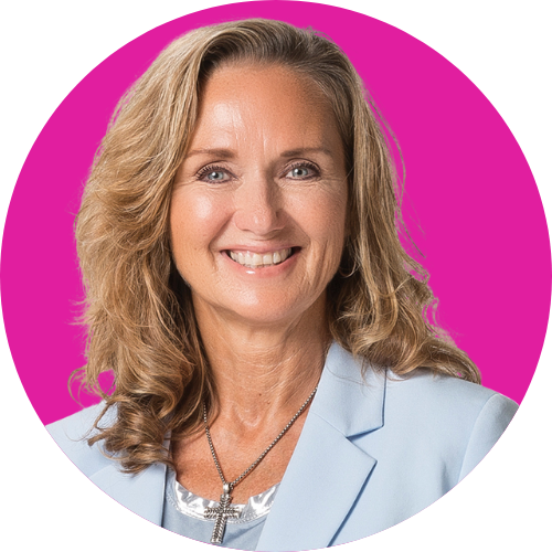 Smiling professional headshot: woman with wavy blonde hair, wearing a light blue blazer and cross necklace, against a bright pink circular background.