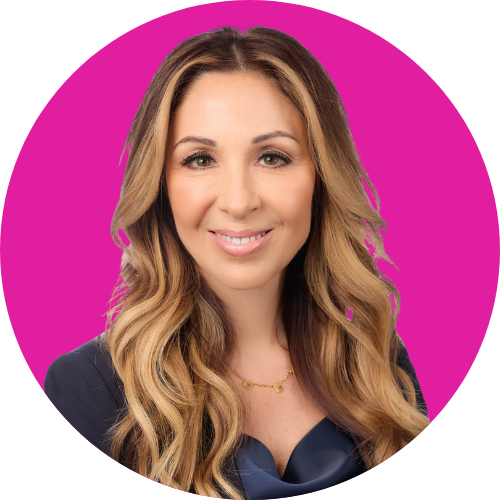 Head-and-shoulders portrait of a smiling woman with long wavy brown hair, wearing a dark blazer, against a bright pink circular background.