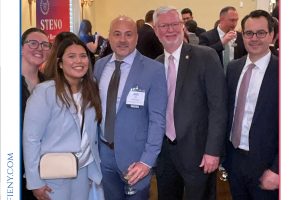 Four professionals in suits posing together at a formal legal awards event, badges visible, with banners and crowd in the background.