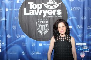 Woman in a black patterned dress posing in front of a blue 'Top Lawyers of Long Island' backdrop at a formal event.
