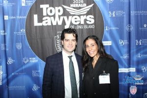 Two formally dressed individuals pose together at a blue 'Top Lawyers' backdrop event, smiling at the camera.