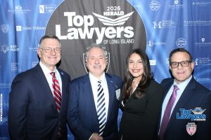 Four professionals in business attire pose for a photo at the 2026 Top Lawyers of Long Island event in front of a blue sponsor backdrop.