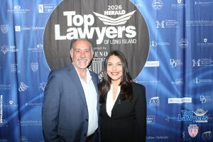 Two smiling professionals pose in front of a blue 'Top Lawyers of Long Island' backdrop at a 2026 event.