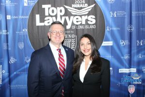 Two smiling professionals pose for a photo in front of a blue 'Top Lawyers of Long Island' backdrop at a formal event.