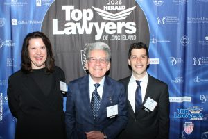 Three professionally dressed individuals posing for a photo at a 'Top Lawyers of Long Island' event in front of a blue sponsor backdrop.