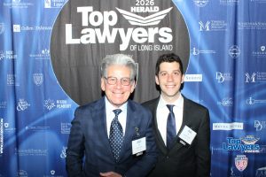 Two men in suits posing and smiling in front of a 'Top Lawyers of Long Island' backdrop at a formal event