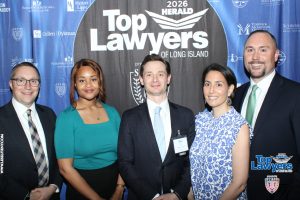 Five professionally dressed people posing in front of a 'Top Lawyers of Long Island' backdrop at a formal event.