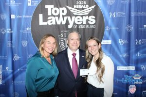 Three smiling people pose for a photo in front of a blue sponsor backdrop at the Top Lawyers of Long Island event.