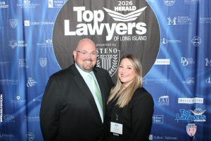 Two smiling professionals pose in front of a blue 'Top Lawyers of Long Island' backdrop at an event.