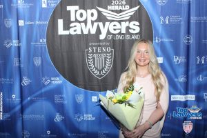Woman holding a bouquet poses in front of a blue 'Top Lawyers of Long Island' backdrop at a formal event.