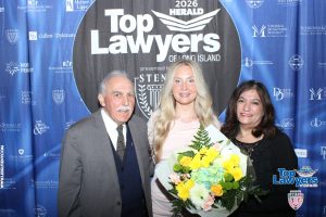 Three people pose for a photo at a Top Lawyers of Long Island event, backdrop filled with sponsor logos; the center woman holds a bouquet of flowers.