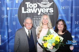 Three people pose together at a Top Lawyers event backdrop; an older man in a gray suit, a smiling blonde woman with a bouquet, and another smiling woman on the right.