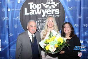 Three people pose for a photo at a Top Lawyers of Long Island event; the woman in the center holds a yellow bouquet, flanked by an older man and another woman against a blue sponsor backdrop.