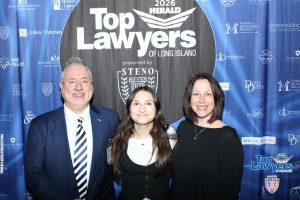 Three smiling people in formal attire pose in front of a blue 'Top Lawyers of Long Island' event backdrop with sponsor logos.