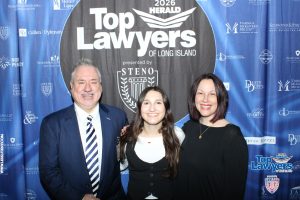 Three smiling people pose together in front of a blue 'Top Lawyers of Long Island' backdrop at a law event.