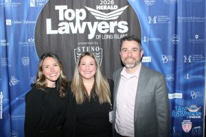 Three smiling professionals posing at a law event in front of a blue 'Top Lawyers of Long Island' backdrop with sponsor logos.