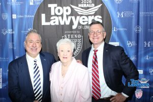 Three professionally dressed individuals pose together at a 'Top Lawyers' event against a blue sponsor backdrop.