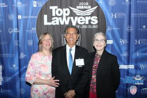 Three professionally dressed people pose and smile at a 'Top Lawyers' event backdrop (2026 Long Island).