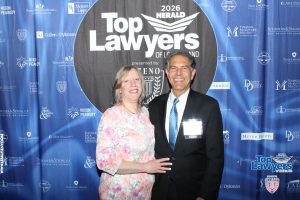 Smiling couple posing in front of a blue 'Top Lawyers' backdrop with sponsor logos; man in a suit with an 'Honoree' badge beside a woman in a floral dress, at the 2026 event.