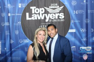 Smiling couple posing together in front of a large circular 'Top Lawyers of Long Island' banner at a sponsored event.