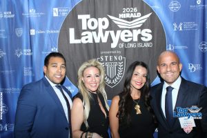 Four professionally dressed individuals pose for a photo at the 2026 Top Lawyers of Long Island event in front of a blue backdrop full of sponsor logos and a large Top Lawyers banner.