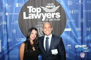 Two well-dressed people smile at a photo backdrop reading 'Top Lawyers of Long Island' with sponsor logos surrounding them.