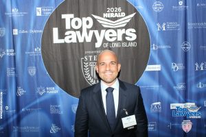 Man in a dark suit posing in front of a blue 'Top Lawyers of Long Island' backdrop at a formal event.