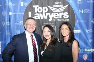Three smiling adults pose for a photo at the Top Lawyers of Long Island event in front of a blue sponsor banner.