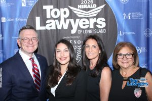 Four smiling professionals posing together at a 'Top Lawyers of Long Island' event in front of a blue sponsor backdrop.