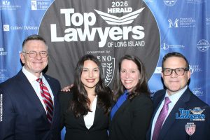 Four people in business attire pose and smile in front of a blue 'Top Lawyers of Long Island' backdrop (2026).