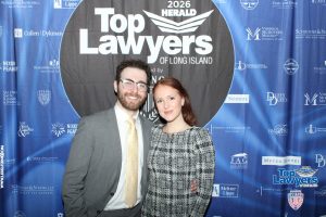 Man and woman pose together in front of a blue 'Top Lawyers of Long Island' backdrop, smiling at the camera.