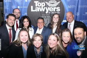 Group of professionally dressed people posing for a photo at a 'Top Lawyers of Long Island' event. banners in blue behind them.