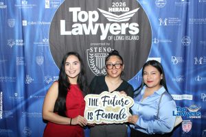 Three women pose at a 'Top Lawyers of Long Island' event, holding a sign that reads 'The Future is Female' with sponsor banners in the background.