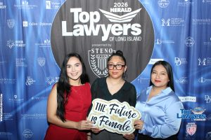 Three women posing at a Top Lawyers of Long Island event in front of a sponsor backdrop; center holds a 'The Future Is Female' sign.
