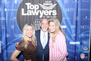 Three smiling adults pose together in front of a blue 'Top Lawyers of Long Island' backdrop at a legal awards event.