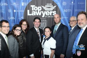 Group of eight professionals in business attire posing for a photo in front of a blue 'Top Lawyers of Long Island' event backdrop.
