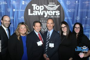 Six professionals in business attire pose together at a Top Lawyers of Long Island event in front of a blue sponsor backdrop with name badges visible.