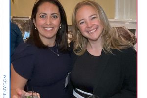 Two smiling women in dark dresses pose with cocktails at a reception for the Top Lawyers of Long Island event.