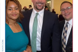 Group photo at a formal event: three smiling professionals in suits, with a chandelier in the background and 'Top Lawyers of Long Island' branding above.