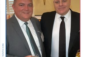 Two men in suits pose for a photo at a formal event, each holding a glass of drink in front of a Top Lawyers banner.