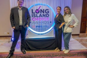 Three people pose and smile at a glow-lit Herald Long Island Choice Awards backdrop featuring a circular blue sign.