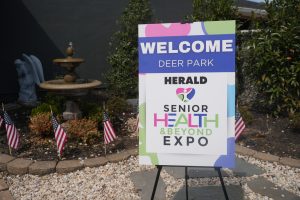 Signboard welcoming visitors to the Senior Health & Beyond Expo at Deer Park; reads WELCOME, DEER PARK, HERALD, and a heart logo with colorful text.