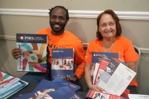 Two people in bright orange shirts sitting at a table and smiling, holding PSEG Long Island brochures and flyers.