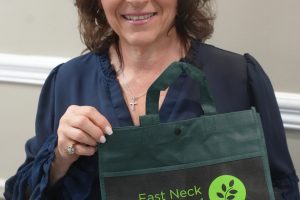 Smiling woman in blue blouse holds a green tote bag with East Neck Nursing and Rehabilitation Center text and logo visible on the front.