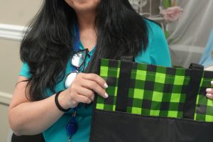 Smiling woman with long black hair in a teal top holds a black-and-green WellCare tote bag.
