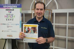 Man in a navy Edward Jones polo holding a flyer about education savings, with a sponsor board in the background.