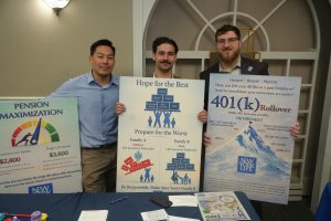 Three men stand indoors holding large retirement-themed posters about pensions and 401(k) rollovers.