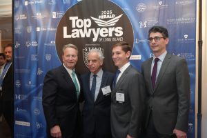 Four men in suits pose for a photo at the 2026 Top Lawyers of Long Island event, with a blue sponsor backdrop behind them.