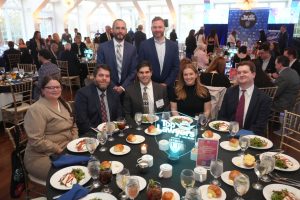 Eight professionals at a formal dinner around a round table, with a glowing 'Top Lawyers of Long Island' centerpiece in the foreground.